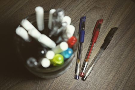 A top view of colorful ballpens in a glass jar on a wooden table.